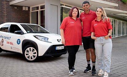 Drei Menschen aus dem Team der Pflegegruppe Nord vor einem Auto der Katholischen Sozialstation Stuttgart