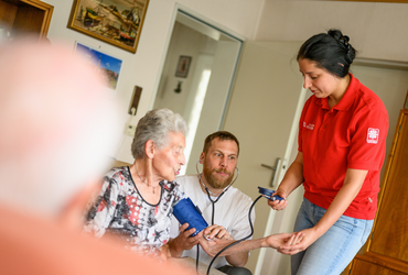 Zwei Pflegekräfte beim Blutdruckmessen bei einer Patientin zuhause